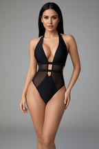 Person wearing a black swimsuit with mesh panels, holding a glass of water.